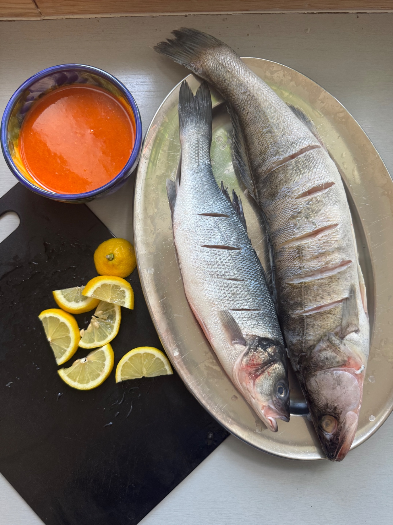 Två hela fiskar på ett silverfat med skivad citron och en skål piri-piri-marinad