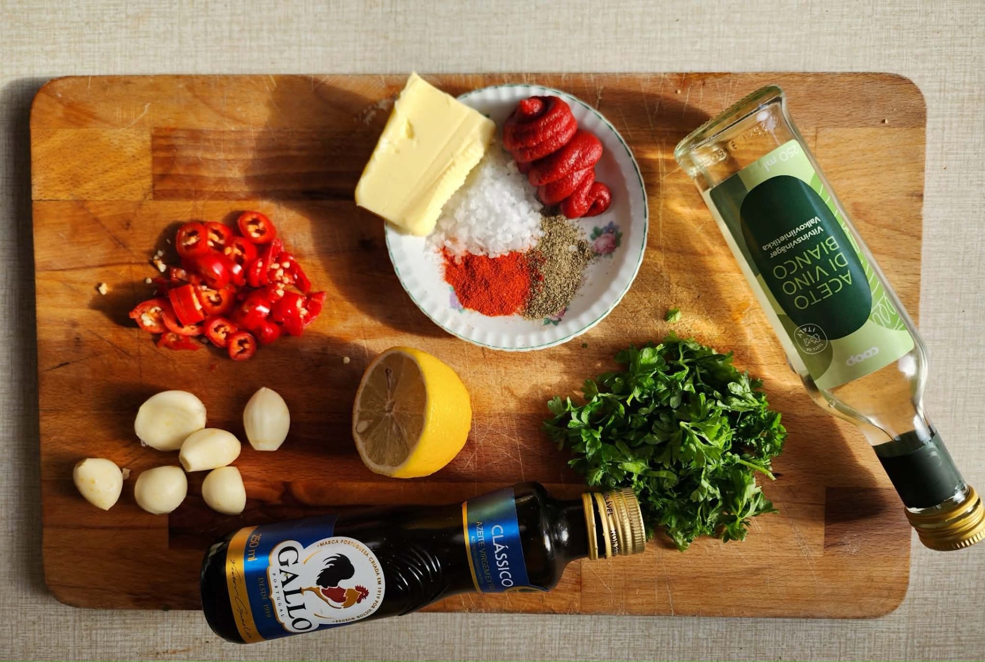 Olivolja, vitvinsvinäger, vitlök, chili, citron, persilja och kryddor på en skärbräda