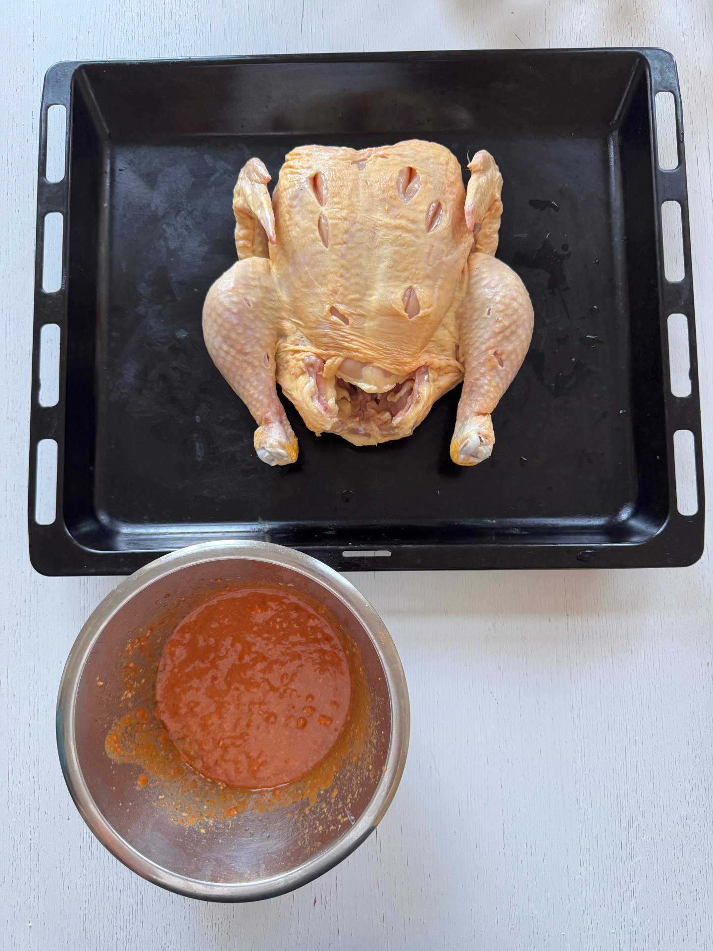 Hel rå kyckling på plåt bredvid skål med piri-piri-marinad