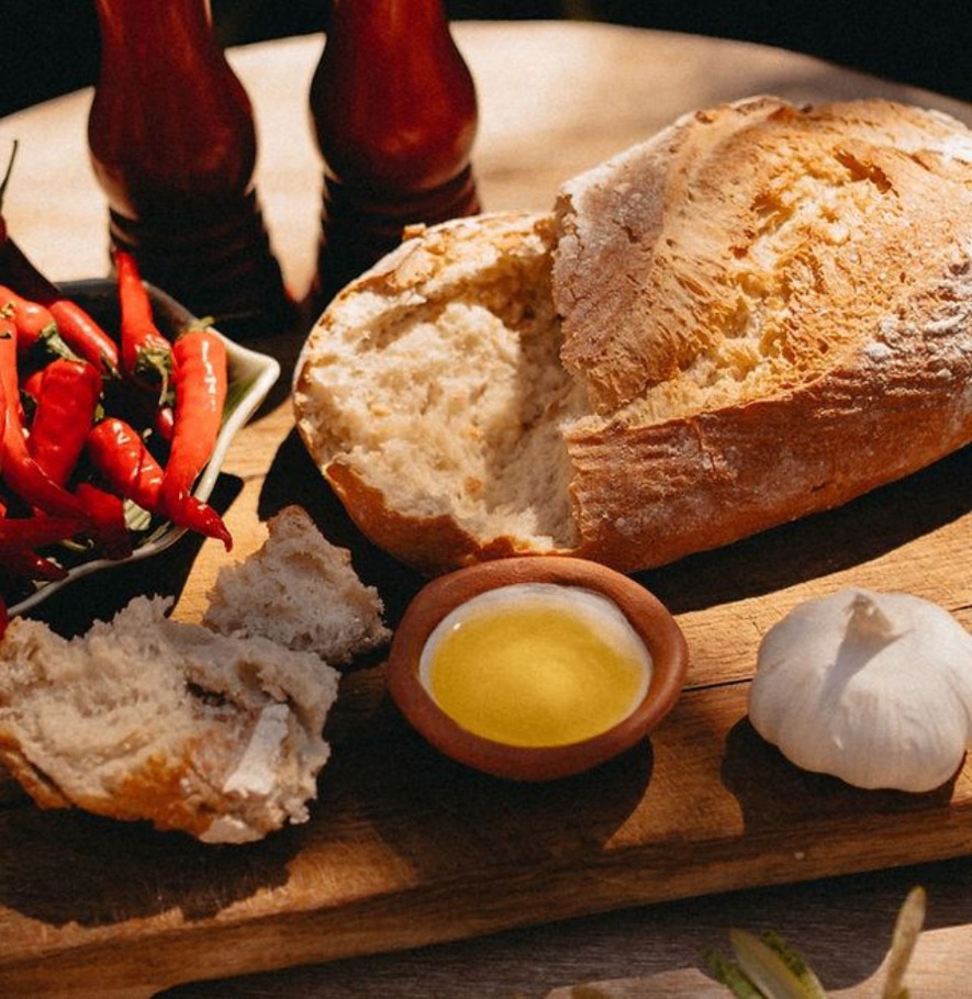Nybakat bröd, olivolja i lerskål, vitlök och röd piri-piri på träbräda