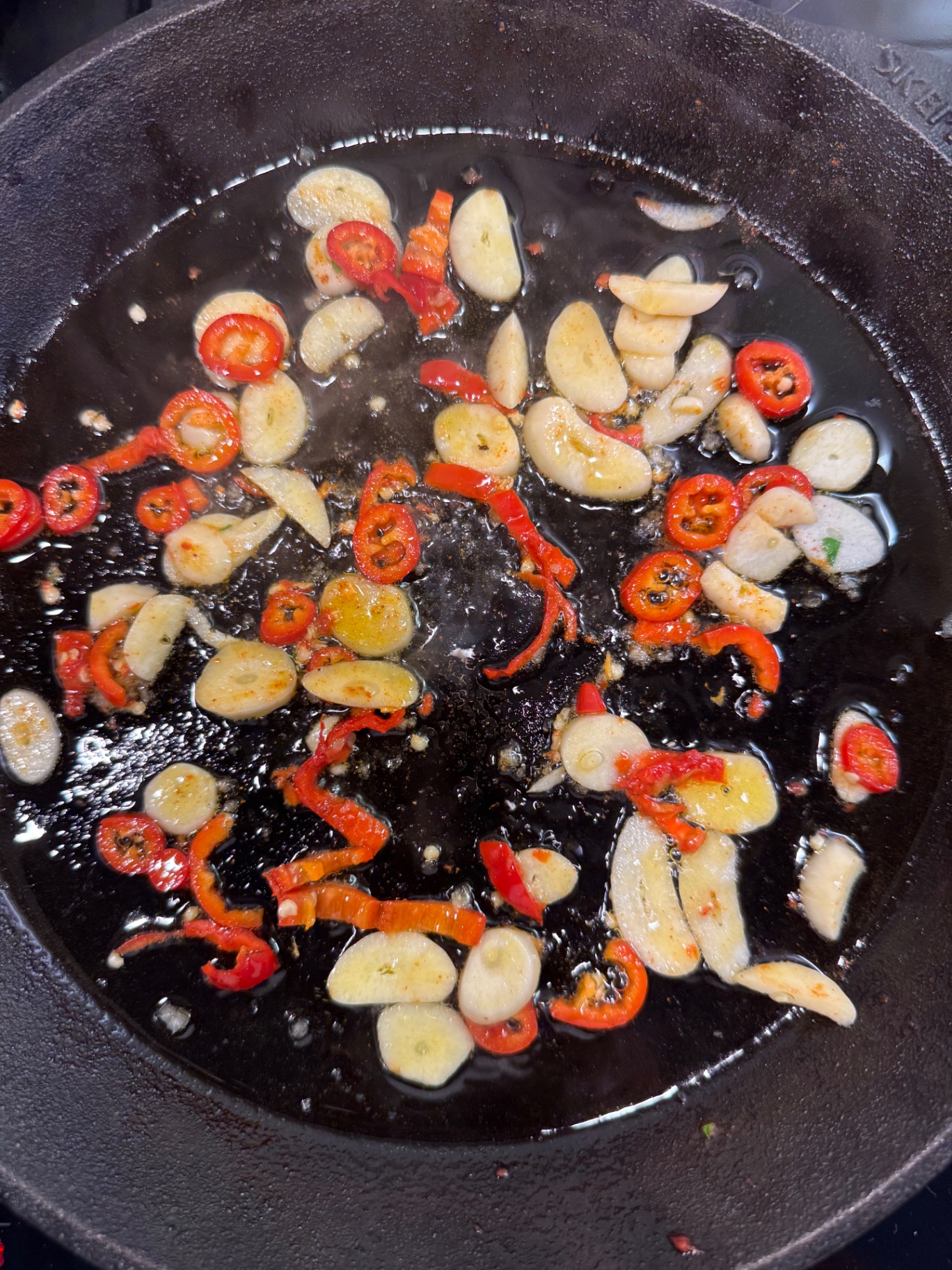 Vitlöksskivor och chili som fräser i het olja i en gjutjärnspanna